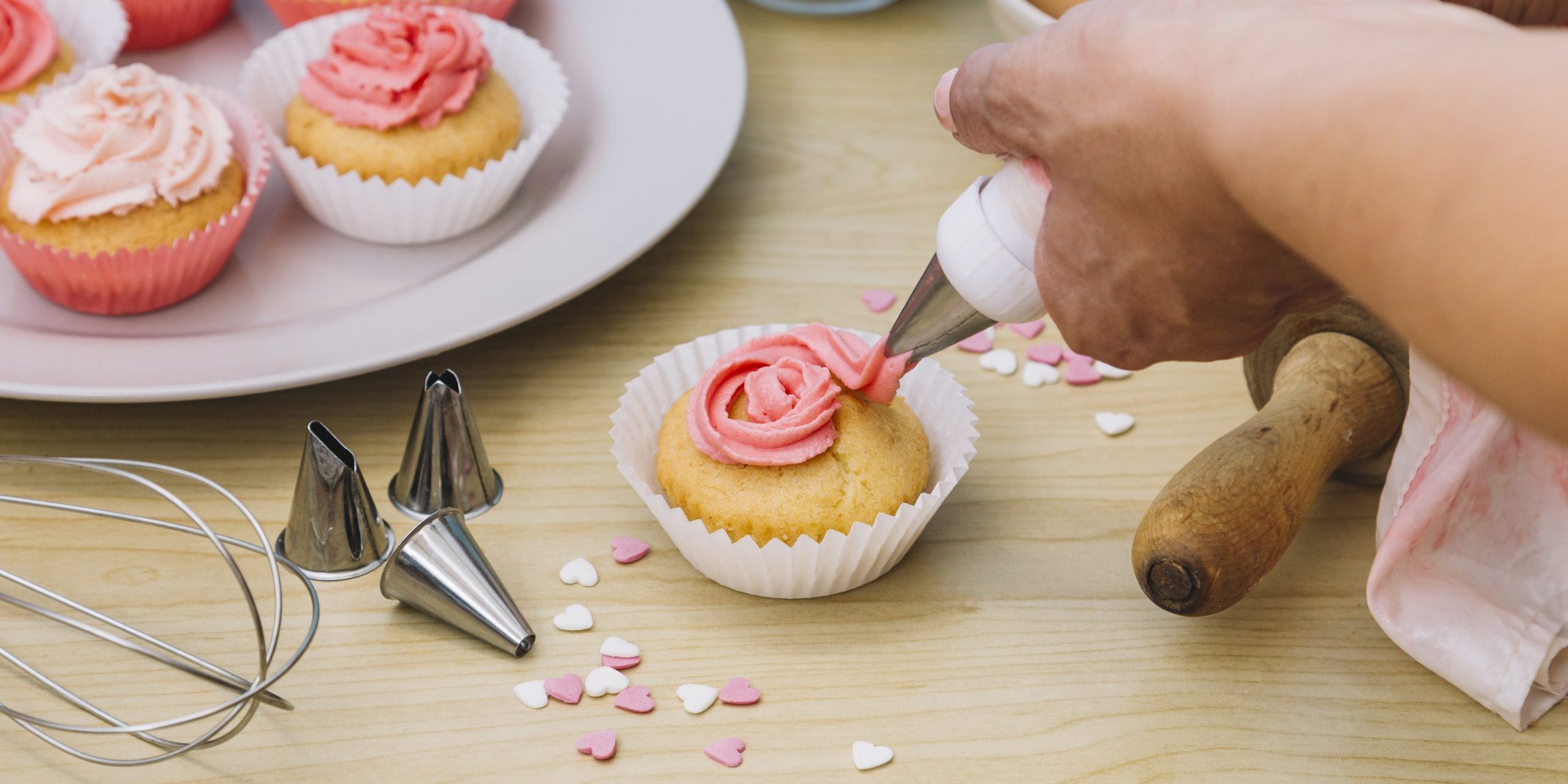 baker-decorates-muffins-with-cream-wooden-desk