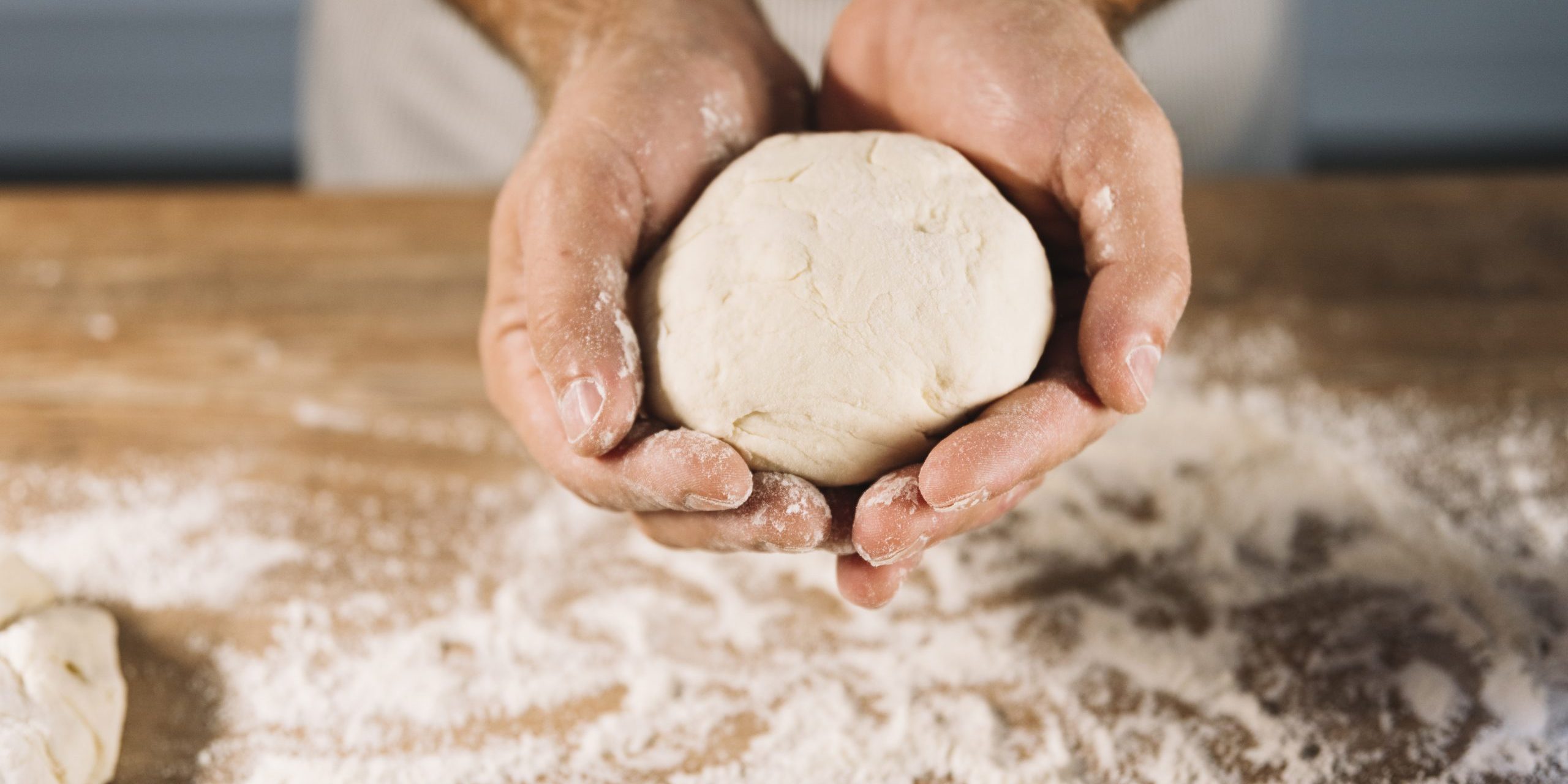 close-up-male-baker-holding-knead-dough-hand-wooden-table